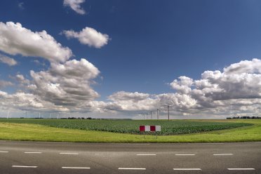 Een autoweg op de voorgrond en grasveld met windmolens op de achtergrond.