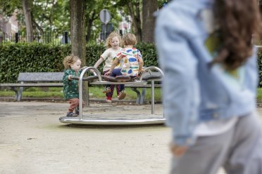 Afbeelding van drie kinderen die op een speeltoestel spelen en een kind op de voorgrond die daar naartoe loopt.