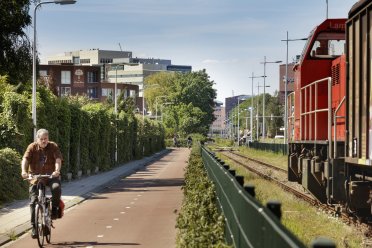 Afbeelding van een fietsende man op het fietspad met een spoor ernaast waar een trein op rijdt.